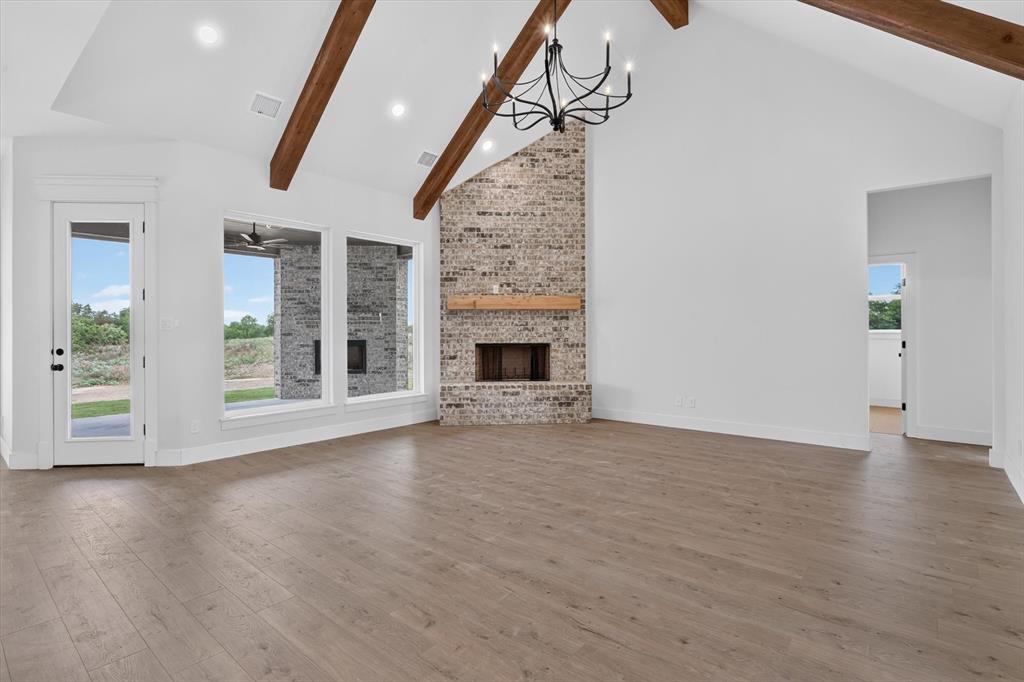 471 Red Bird Drive Springtown, TX 76082 - Photo 7 of 35 Spacious room featuring vaulted ceilings with exposed wood beams, a brick fireplace with a wood mantle, and wood-finish flooring