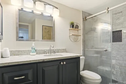 a bathroom with a granite countertop shower sink vanity mirror and toilet