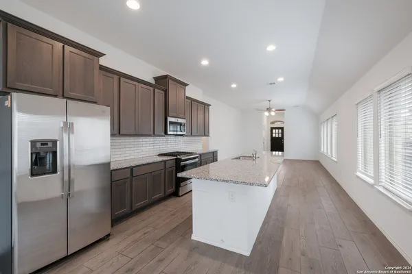a large kitchen with stainless steel appliances granite countertop a refrigerator a sink dishwasher a stove and a microwave oven on the wooden floor