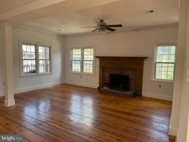 a view of an empty room with wooden floor fireplace and a window