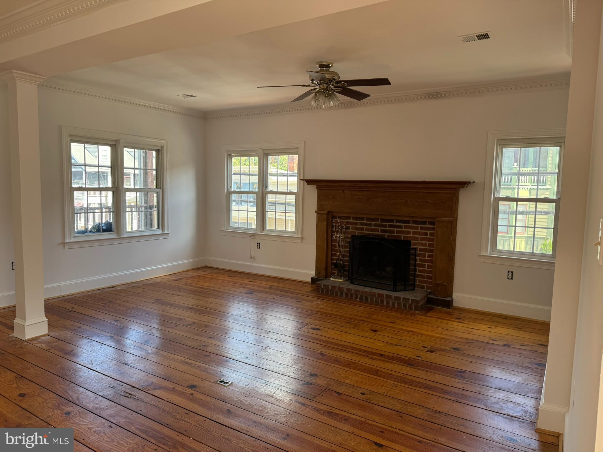 a view of an empty room with wooden floor fireplace and a window