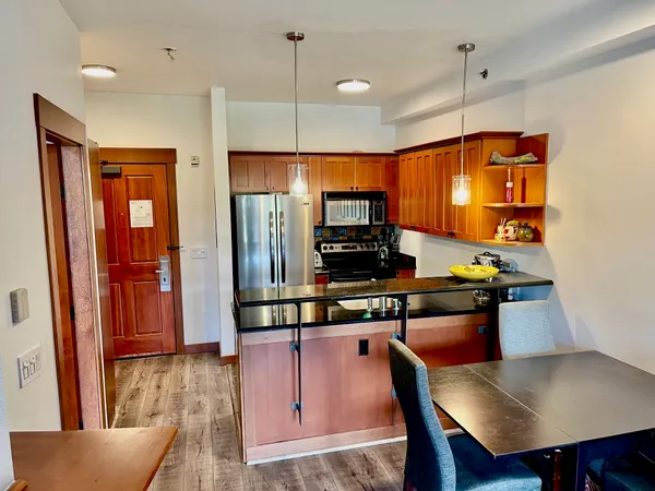 a kitchen with stainless steel appliances kitchen island granite countertop a refrigerator a stove top oven a dining table and chairs with wooden floor