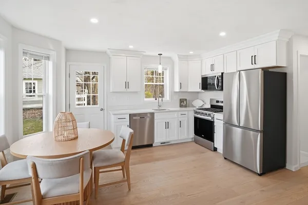 a kitchen with stainless steel appliances granite countertop a dining table chairs refrigerator and microwave