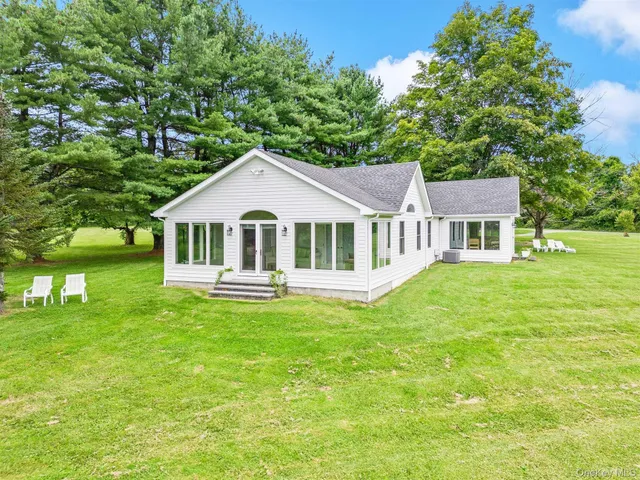 a white house sitting in middle of a big yard with large trees