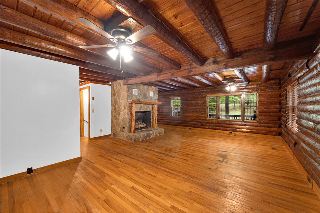 237 Spring Valley Road Liberty, SC 29657 - Photo 5 of 50 A spacious log cabin interior with natural wood walls, ceiling beams, and gleaming hardwood floors, centered by a stone fireplace.