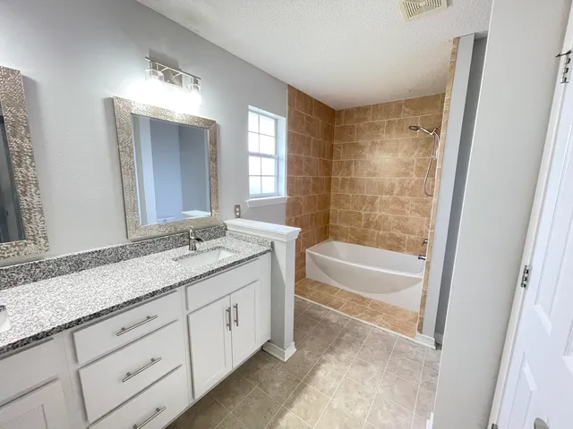 a bathroom with a granite countertop sink a mirror a bathtub and shower