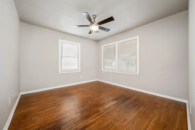 an empty room with wooden floor ceiling fan and windows