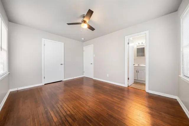 an empty room with wooden floor ceiling fan and windows