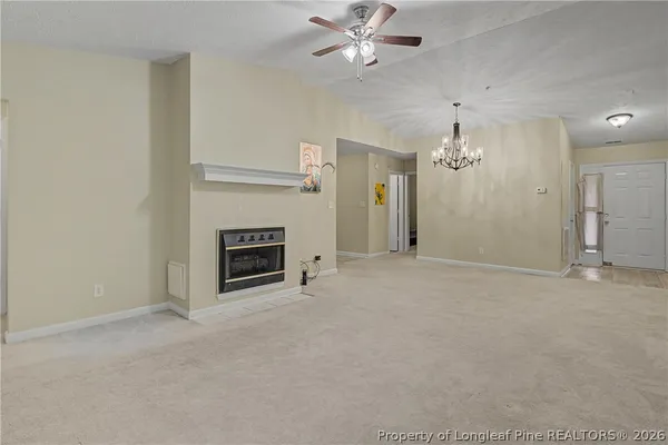 an empty room with chandelier fan and fireplace
