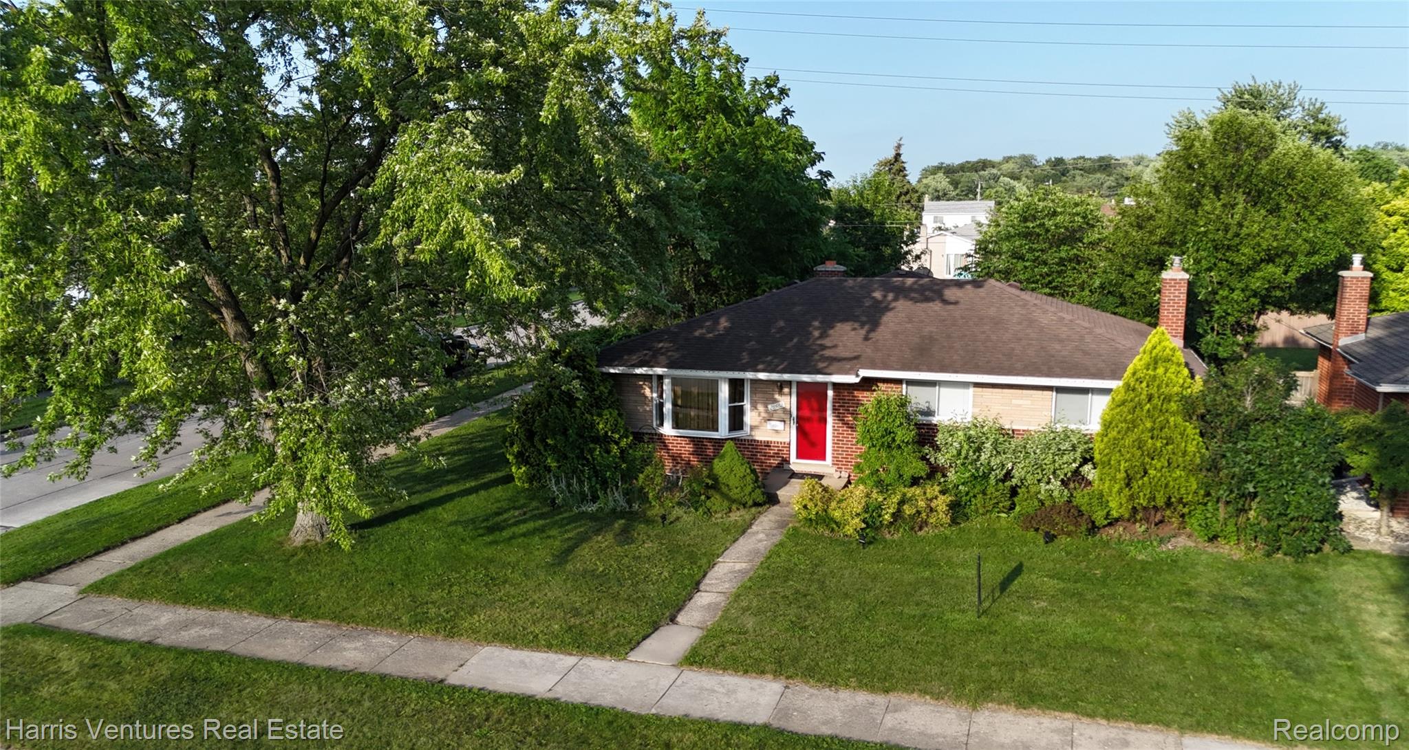 28482 Sutherland Avenue Warren, MI 48088 - Photo 4 of 25 Brick facade residence with a red entry door, framed by mature trees and established landscaping