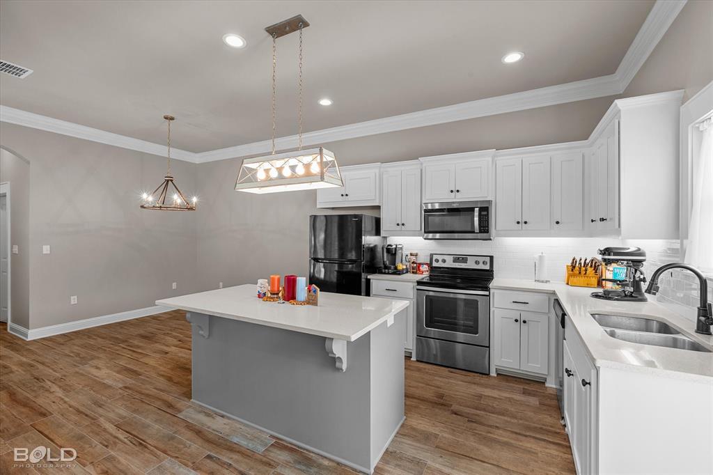 6896 Bethany Reed Circle Blanchard, LA 71107 - Photo 20 of 37 Kitchen featuring white shaker cabinetry, stainless steel appliances, a center island with a light-toned countertop, wood-finish flooring, and crown molding