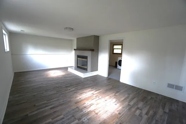 a view of an empty room with wooden floor fireplace and a window