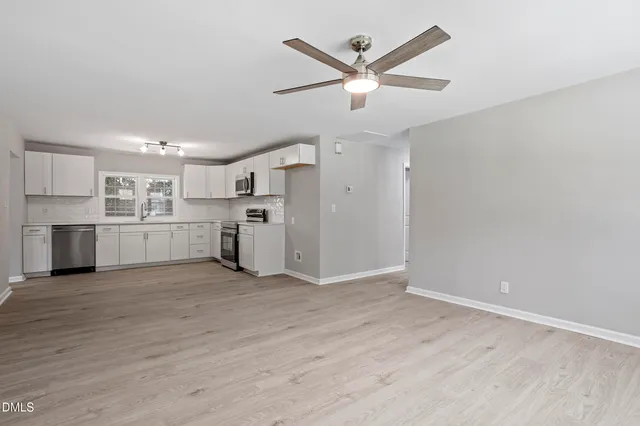 an empty room with wooden floor ceiling fan and windows