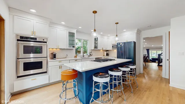 a kitchen with stainless steel appliances kitchen island granite countertop a stove a refrigerator a oven a sink a dining table and chairs with wooden floor