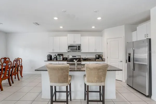 a kitchen with stainless steel appliances granite countertop a dining table chairs refrigerator and sink