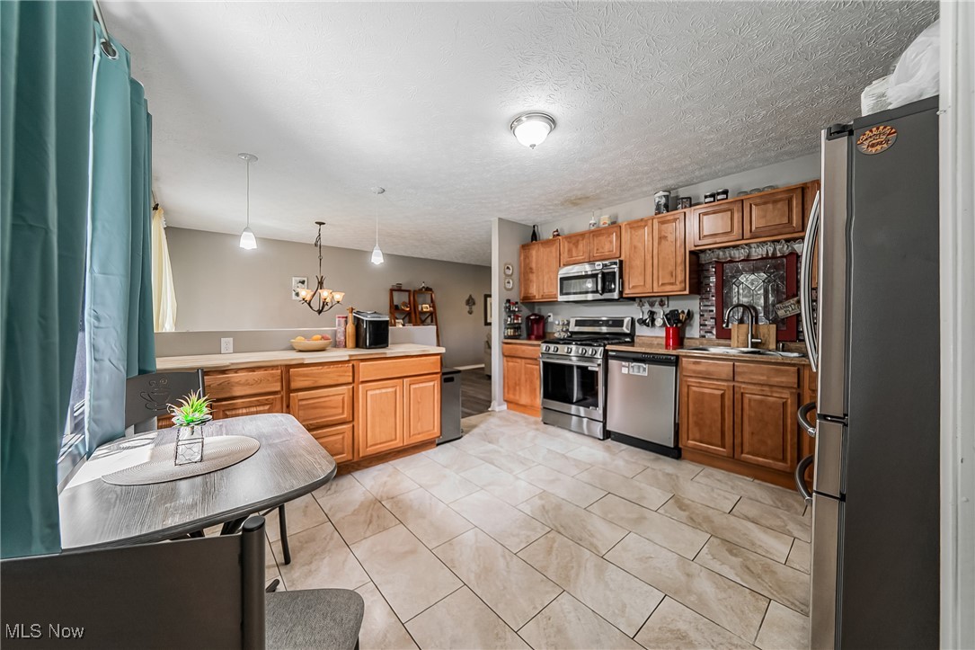 10794 Waterfall Road Strongsville, OH 44149 - Photo 13 of 37 Kitchen with appliances with stainless steel finishes, pendant lighting, a textured ceiling, a chandelier, and brown cabinets
