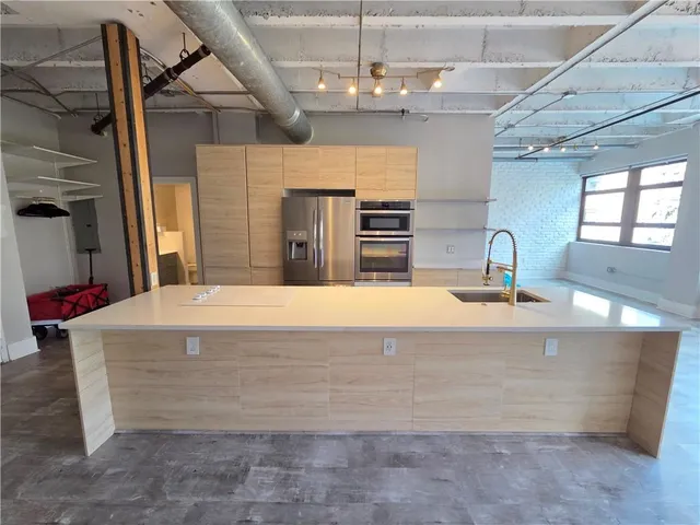 a view of a kitchen with kitchen island a sink stainless steel appliances wooden floor and chair