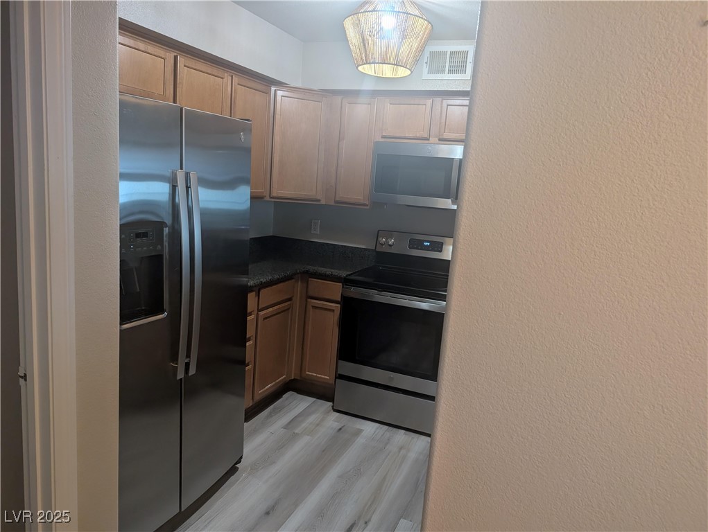 3145 East Flamingo Road, Unit 1123 Las Vegas, NV 89121 - Photo 13 of 30 Kitchen with appliances with stainless steel finishes, dark countertops, a textured wall, light wood-style floors, and hanging light fixtures