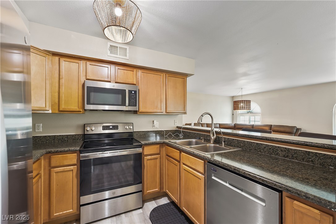 3145 East Flamingo Road, Unit 1123 Las Vegas, NV 89121 - Photo 10 of 30 Kitchen featuring stainless steel appliances, light wood-type flooring, pendant lighting, and brown cabinets