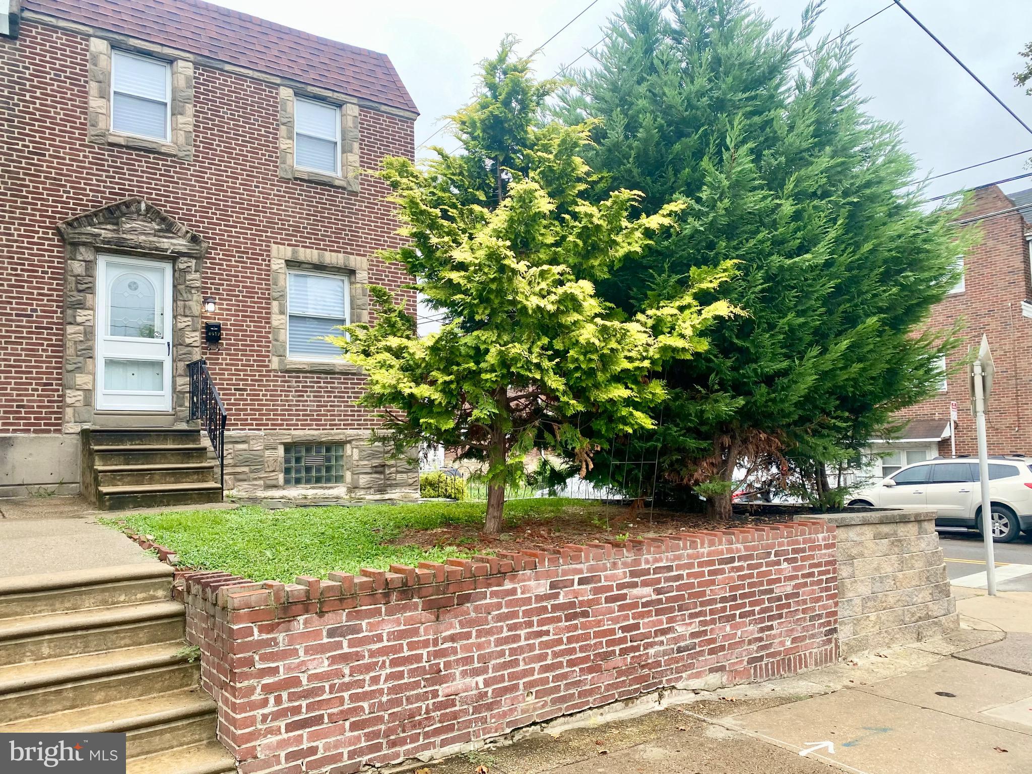 a view of a brick house with a yard plants and large tree