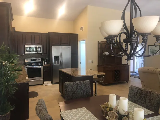 a kitchen with stainless steel appliances kitchen island granite countertop a stove a refrigerator a sink a dining table and chairs with wooden floor