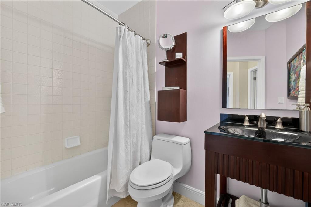8420 Excalibur Circle, Unit R7 Naples, FL 34108 - Photo 22 of 24 Bathroom featuring a bathtub with tiled walls, a toilet, and a vanity with a dark countertop and a mirror