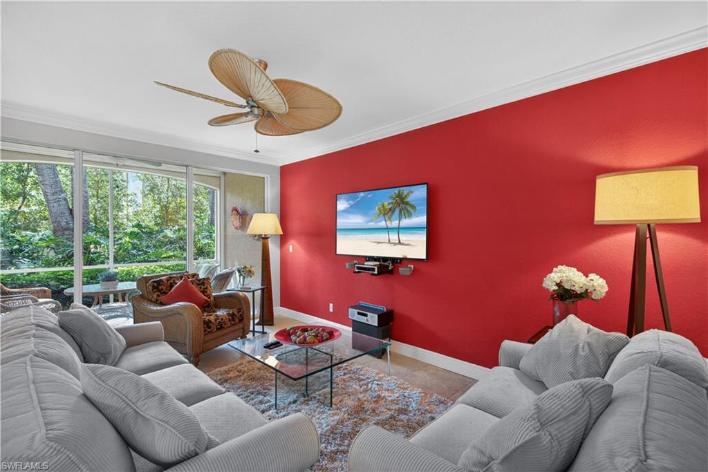 8420 Excalibur Circle, Unit R7 Naples, FL 34108 - Photo 7 of 24 The living area features a bright red accent wall, a ceiling fan, and large windows with views of abundant greenery