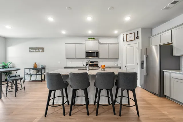 a kitchen with stainless steel appliances granite countertop a dining table chairs refrigerator and cabinets