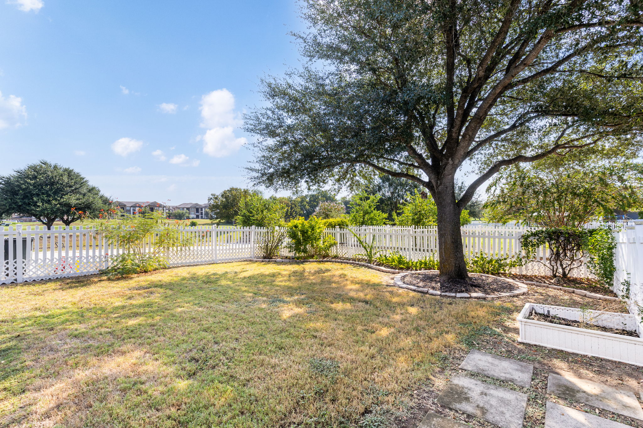 784 Sampson Kyle, TX 78640 - Photo 32 of 40 Mature trees shade a fenced backyard with a stone-paved path under open blue skies.