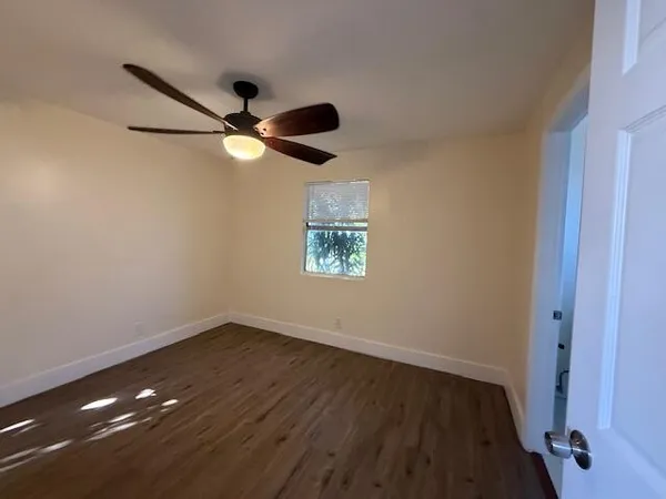 a view of an empty room with wooden floor and a ceiling fan