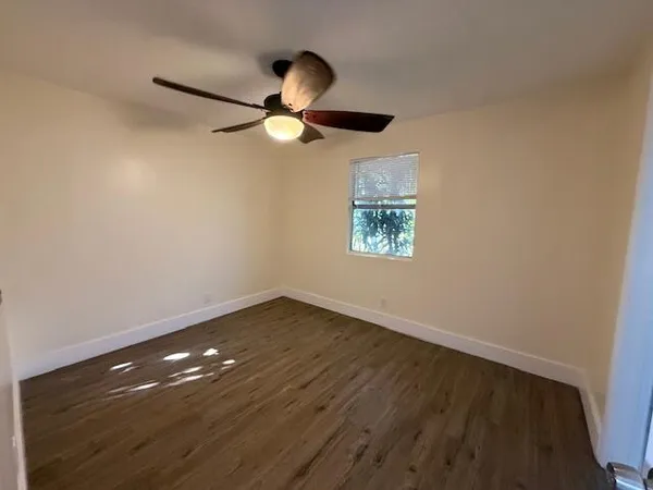 an empty room with wooden floor fan and windows
