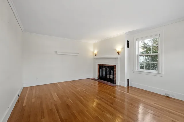 a view of an empty room with wooden floor fireplace and a window