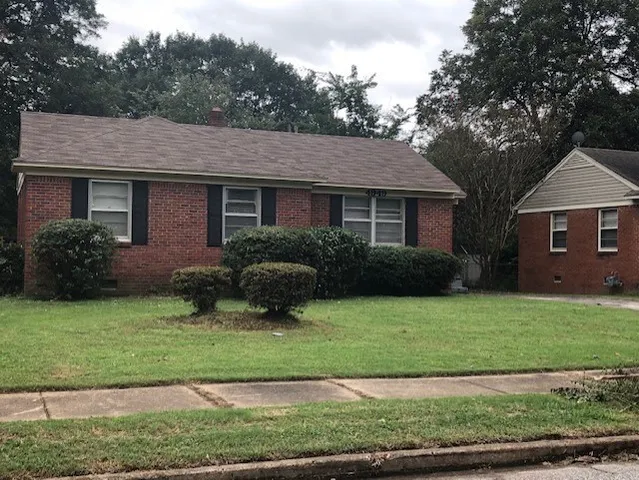 a view of a house with a yard plants and large tree
