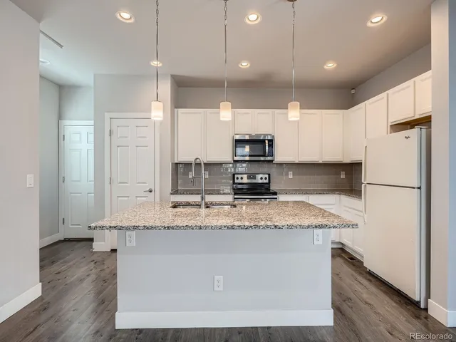 a kitchen with stainless steel appliances granite countertop a refrigerator a sink and white cabinets
