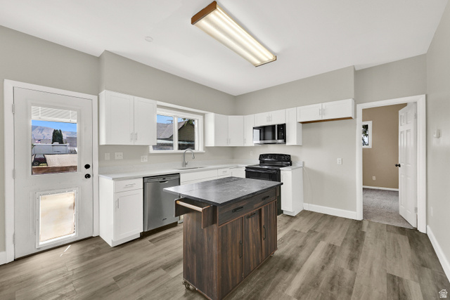 716 East Factory Street Garland, UT 84312 - Photo 14 of 30 Kitchen featuring wood-finish flooring, white cabinetry, stainless steel dishwasher, black range, and a central island with a contrasting wood-finish base and dark countertop