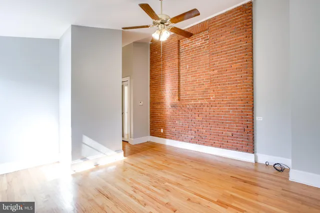 a view of an empty room with wooden floor and a ceiling fan