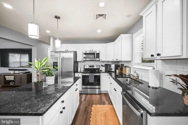a kitchen with stainless steel appliances granite countertop a sink a stove and a wooden floors