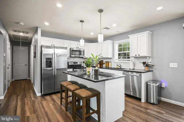 a kitchen with stainless steel appliances kitchen island granite countertop a refrigerator a sink dishwasher a stove and white cabinets with wooden floor