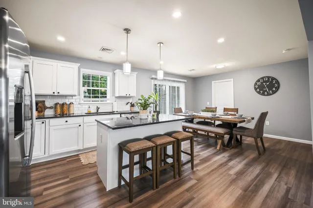 a kitchen with stainless steel appliances granite countertop a stove a refrigerator a kitchen island a dining table and chairs with wooden floor