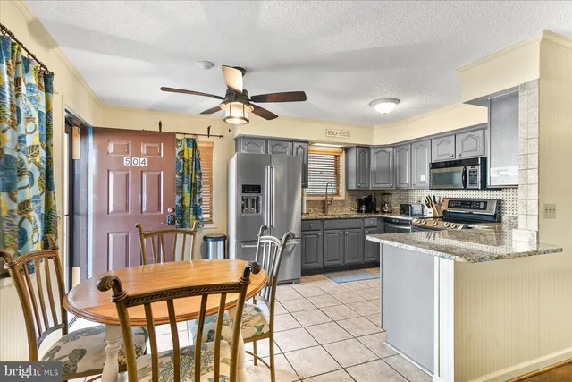 a kitchen with stainless steel appliances kitchen island granite countertop a refrigerator a stove top oven and a dining table with wooden floor