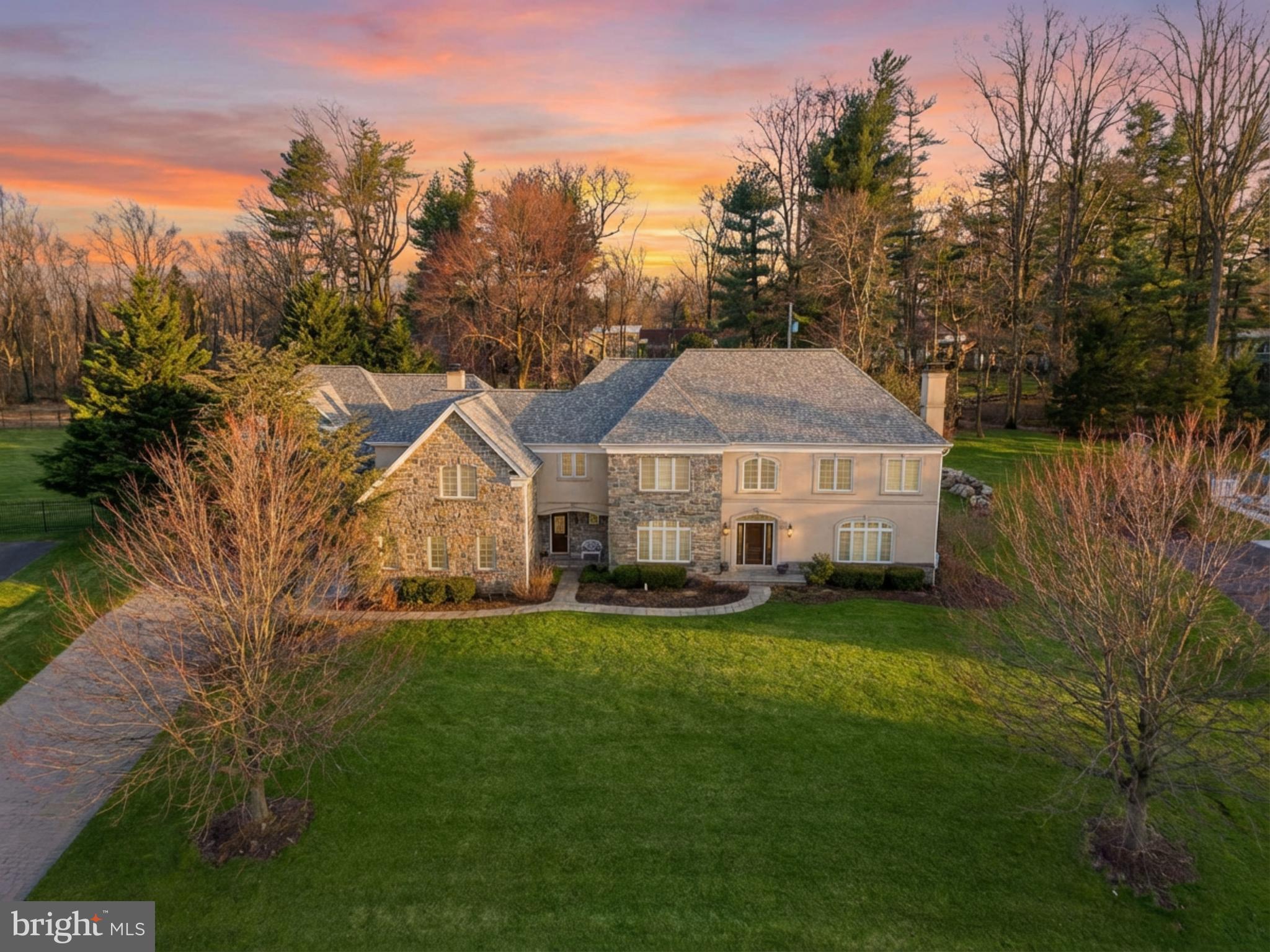 a house that is sitting in the grass with large trees and plants