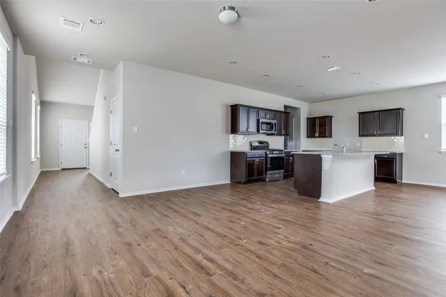 a view of an empty room with kitchen and a window