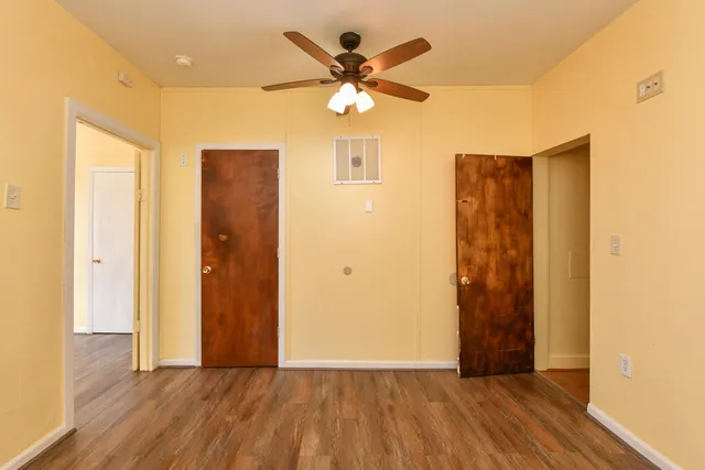 a view of an empty room with wooden floor and a ceiling fan
