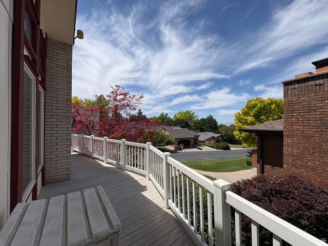 595 Meadowlark Road Orem, UT 84097 - Photo 78 of 87 Spacious outdoor deck with composite decking and white railing, featuring a large window with red trim, light-colored brick exterior, and surrounding mature trees