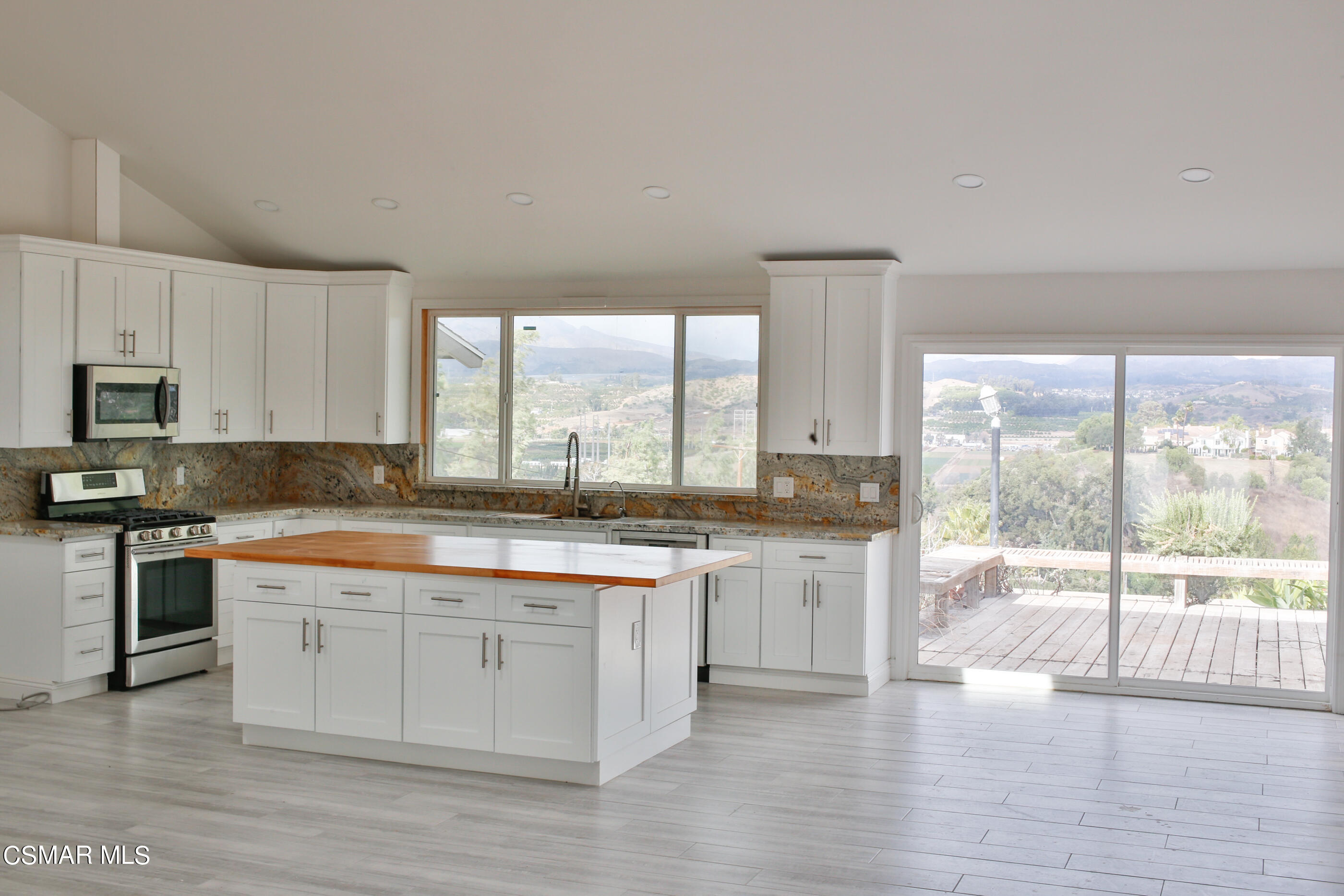 3836 Dalaway Drive Moorpark, CA 93021 - Photo 14 of 29 a large kitchen with granite countertop a stove a sink and white cabinets with wooden floor next to windows