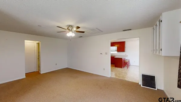an empty room with a ceiling fan and a kitchen