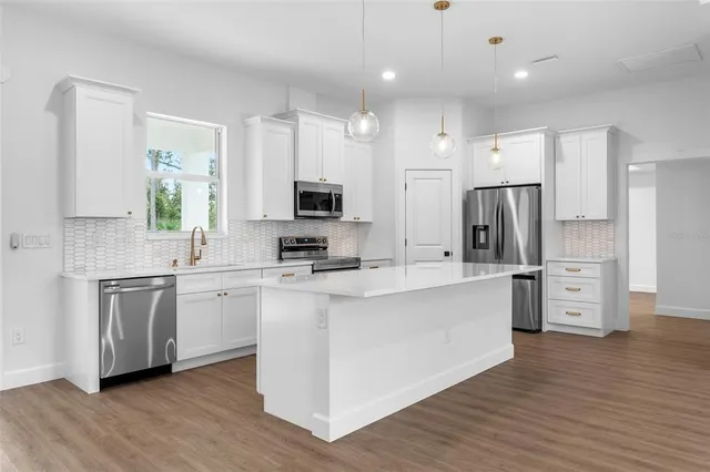 a large kitchen with stainless steel appliances a refrigerator a sink dishwasher a oven and a dining table with wooden floor