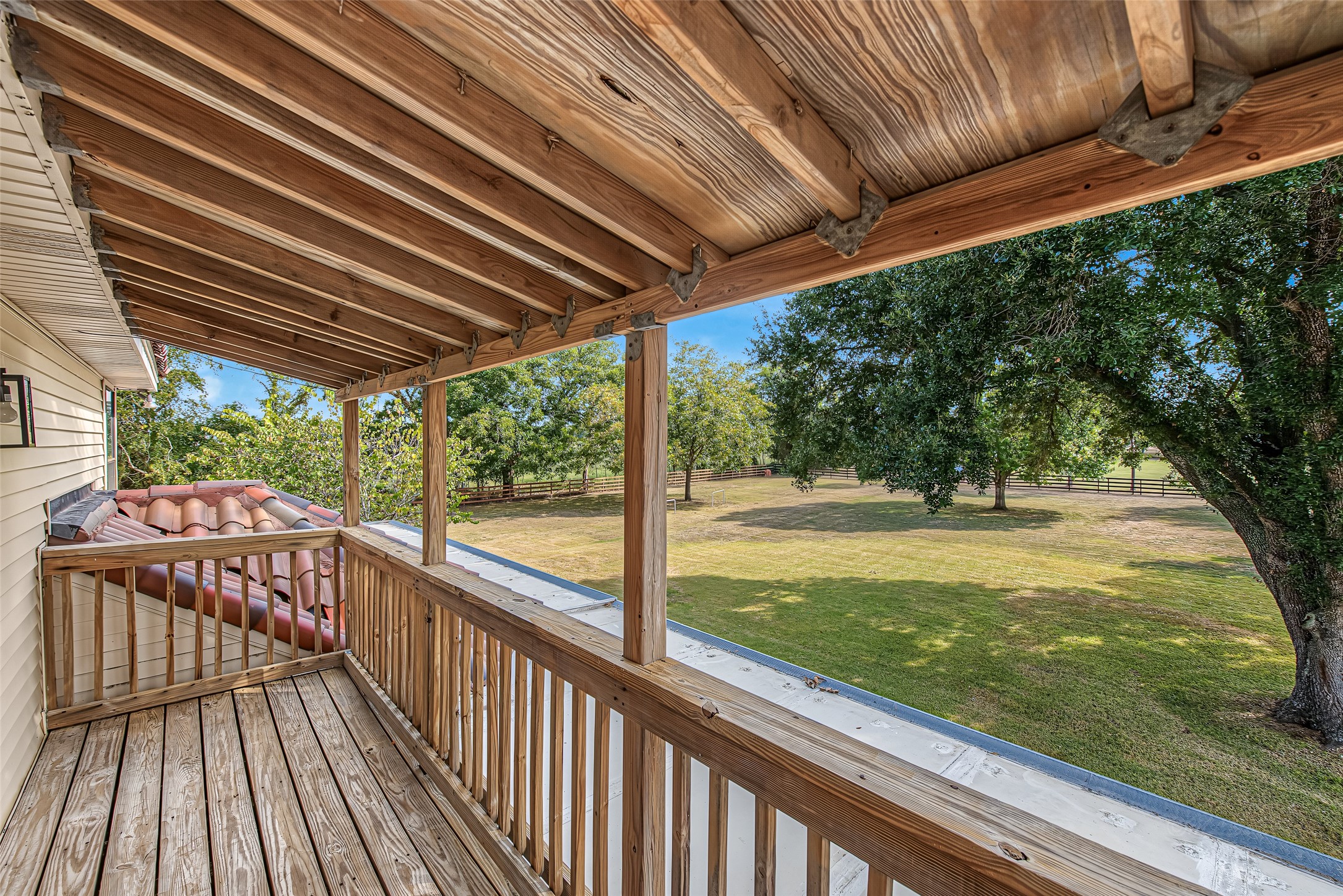 1345 Peach Ridge Road Brookshire, TX 77423 - Photo 44 of 50 Offering an elevated vantage point over the property, this covered second-story wood balcony features exposed timber ceiling joists, wood plank decking, and a sturdy perimeter railing. Directly accessible from the upper living quarters, this private outdoor retreat is shaded for year-round comfort while capturing panoramic views of the lush green acreage, mature shade trees, and surrounding fenced pastures.