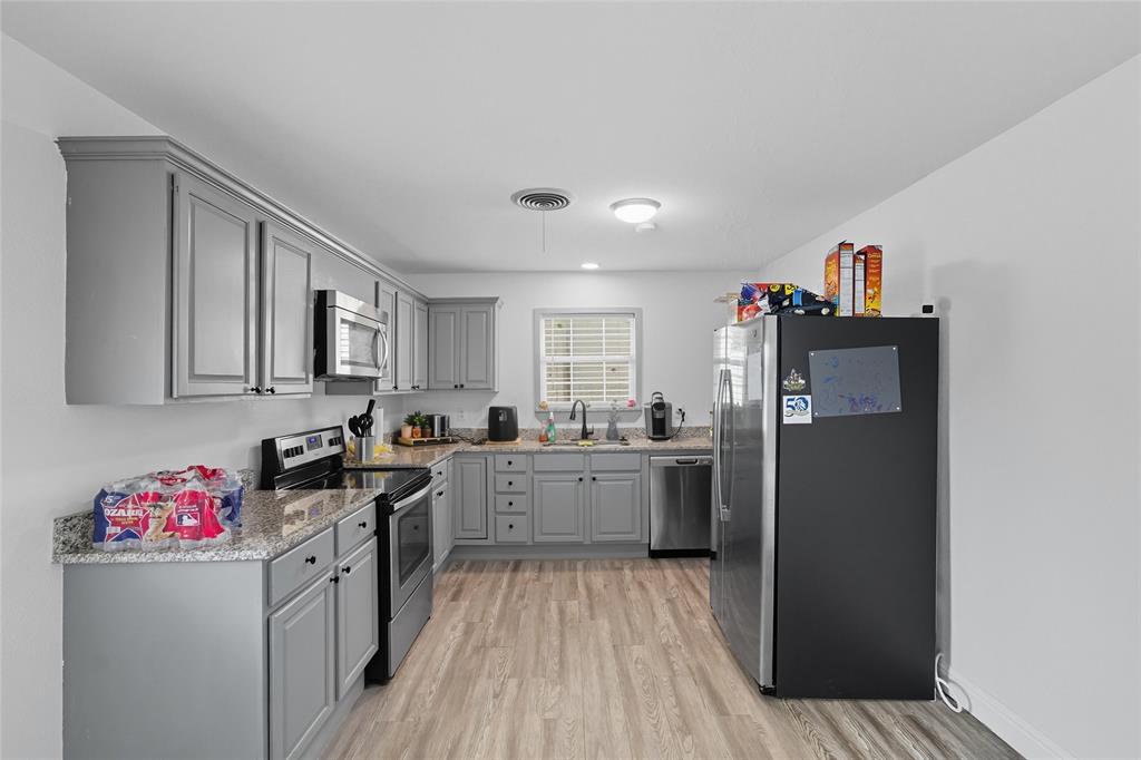 421 East Tarrant Road Grand Prairie, TX 75050 - Photo 18 of 32 Kitchen featuring gray cabinetry, stainless steel appliances, light wood finished floors, and light stone countertops