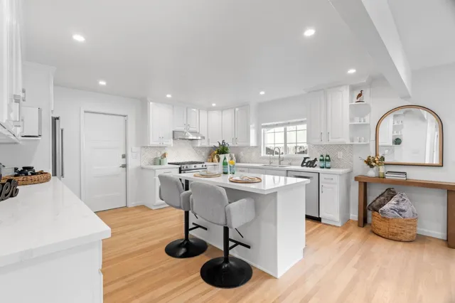 a kitchen with stainless steel appliances granite countertop a refrigerator a sink dishwasher a stove and white cabinets with wooden floor